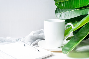 Coffee mug white with green leaves and stationery on wooden table