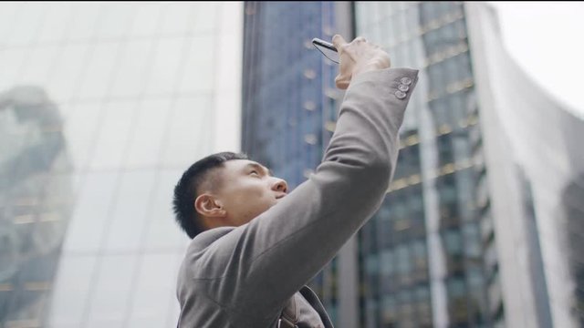 Handsome Asian male in a suit taking a picture with his phone in the city 