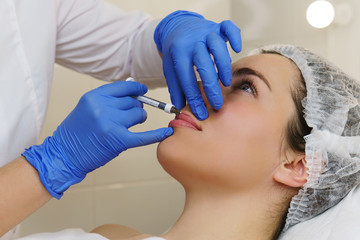 Aesthetic cosmetology. Hands cosmetologist injections of hyaluronic acid in upper lip of girl. Lip...