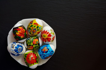 Bright multi-colored Easter eggs with floral pattern in plate on dark background. Symbol of religious holiday.