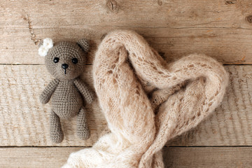 A small knitted baby toy-bear and a warm blanket shaped heart on wooden background, lazy sleepy morning concept, flat lay, top view