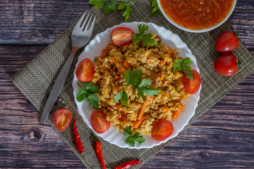 Pilaf and cherry tomatoes in a plate on a wooden background, adjika. Central Asian cuisine. Horizontal orientation. Hot peppers