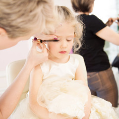 Close up of a portrait of a little girl having make-up applied by a makeup artist. Children's hairdressing salon. Children make up. 