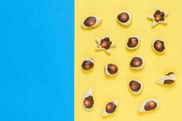 Fototapeta premium Chocolates in the form of sea shellfish and shells on a yellow and blue background. Flat lay.