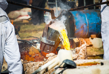 Close-up of blacksmith holding a hot crucible by the iron pliers from furnace and pouring the melting gold into the statue block. The process to making of metal statue in local Thailand traditional.
