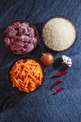 Ingredients for making pilaf, rice, meat, onions and carrots on a dark background