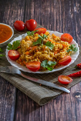 Pilaf and cherry tomatoes in a plate on a wooden background, adjika. Central Asian cuisine. Vertical orientation. Hot peppers