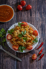 Pilaf and cherry tomatoes in a plate on a wooden background, adjika. Central Asian cuisine. Vertical orientation. Hot peppers