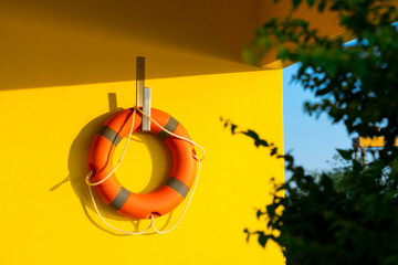 a bright orange life ring hanged against on bright yellow concrete wall