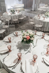 Wine glasses on round Banquet table served. Interior of restaurant for wedding dinner, ready for guests. Decorated with floral arrangement. Dishes, wine glasses and napkins. Catering concept.