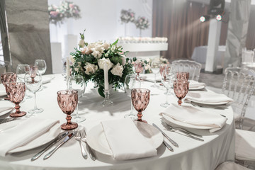 Wine glasses on round Banquet table served. Interior of restaurant for wedding dinner, ready for guests. Decorated with floral arrangement. Dishes, wine glasses and napkins. Catering concept.
