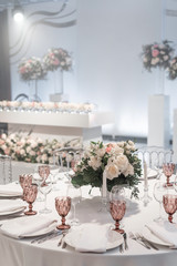 Wine glasses on round Banquet table served. Interior of restaurant for wedding dinner, ready for guests. Decorated with floral arrangement. Dishes, wine glasses and napkins. Catering concept.