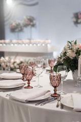 Wine glasses on round Banquet table served. Interior of restaurant for wedding dinner, ready for guests. Decorated with floral arrangement. Dishes, wine glasses and napkins. Catering concept.