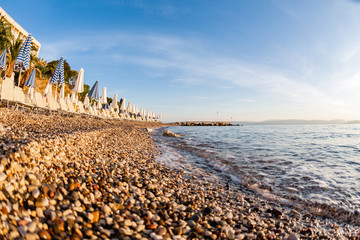 Summer sunrise on coast, Corfu island, Greece. Beach with Sunbeds and umbrellas with perfect views of the mainland Greece mountains.