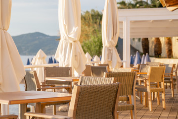 Tables in cafe. Summer sunrise on coast, Corfu island, Greece. Beach with Sunbeds and umbrellas with perfect views of the mainland Greece mountains.