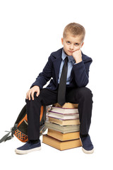 Cute sad schoolboy sitting on a stack of books. Isolated on a white background. Vertical.