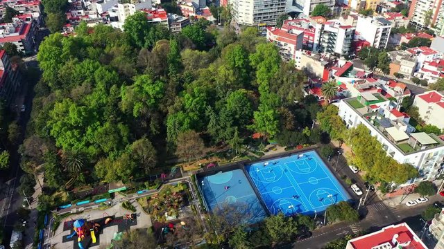 DRONE FLIGHT OVER PARK IN MEXICO CITY RESIDENTIAL AREA. KIDS PLAYGROUND COLORFUL, BLUE BASKETBALL COURT, AND CITY STABLISH