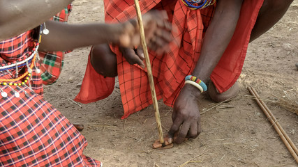 two maasai men use a hand drill to start a fire at a manyatta in kenya