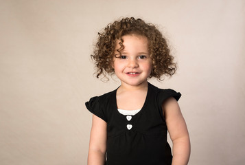 Smiling toddler with brown curly hair isolated on beige background