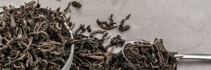 Dried tea in a white ceramic cup with a spoon on a gray textured background.