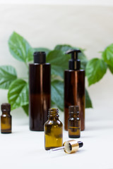 Dark cosmetic bottles and green natural leaves on a light background. Copy space Beauty salon blogger, salon therapy, minimalist concept. The concept of natural environmentally friendly cosmetics.