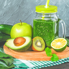 healthy green smoothie with ingredients on a wooden table: apple, kiwi, lime, spinach, mint, avocado, cucumber