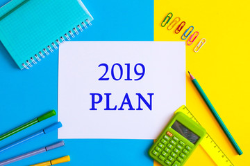 Top view of 2019 PLAN text on white paper note with business office accessories.Top view.Copy space. School office supplies.Creative desk with colourful stationery.Colored paper clip.Planning concept.