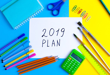 Top view of 2019 PLAN text on white paper note with business office accessories.Top view.Copy space. School office supplies.Creative desk with colourful stationery.Colored paper clip.Planning concept.