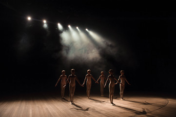 A group of small ballet dancers rehearses on stage with light and smoke