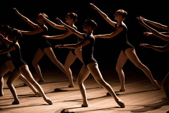 A choreographed dance of a group of graceful pretty young ballerinas practicing on stage in a classical ballet school