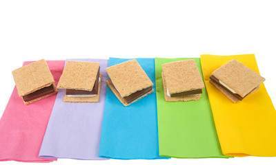 top view of many s'mores lined up in a row on colorful napkins, ready for campfire party. Popular treat for Girl Scouts.