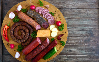 Big set with sausages. Many kinds of sausage, smoked cheese, fresh vegetables on a wooden tray....