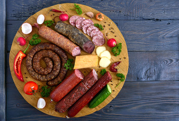 Big set with sausages. Many kinds of sausage, smoked cheese, fresh vegetables on a wooden tray....