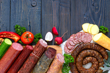 Many kinds of sausage, smoked cheese, fresh vegetables on a wooden background. Products to the...