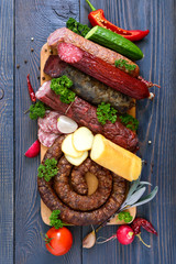 Many kinds of sausage, smoked cheese, fresh vegetables on a wooden background. Products to the holiday. Top view. Flat lay.
