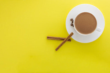 Obraz na płótnie Canvas White cup of hot coffee and Cinnamon sticks isolated on yellow background.