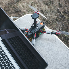 FPV drone lies on the table near the laptop and control panel.