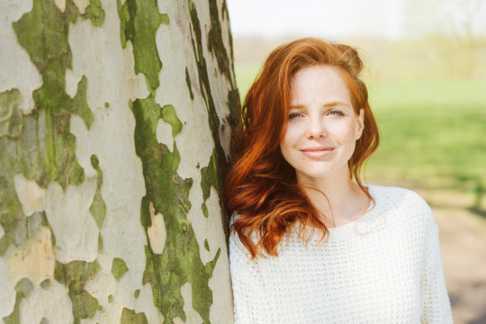 Cheerful young redhead woman leaning on a tree