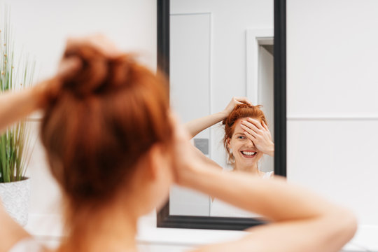 Laughing young woman looking at herself in mirror