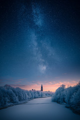 Majestic milky way over a clock tower and icy river at winter