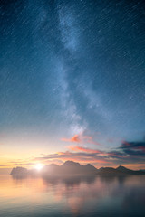 Beautiful vertical view of an ocean and mountains with epic milky way on the sky and star trail...
