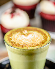 A close up view of a latte art heart on top of a green matcha chai coffee in a drinking glass