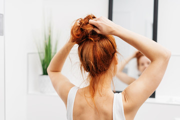 Young redhead woman tying her hair up in a bun - Powered by Adobe