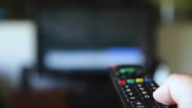 Hand Using Tv Remote To Change The Channel On Televison. Person searching through televison programs with remote control. Close up tv remote. Shallow depth of field.