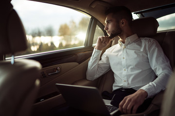 Man looking away while sitting on the back seat of a car, businessman in taxi - obrazy, fototapety, plakaty