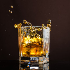 hexagonal glass of whiskey with ice and splashes from an abandoned and falling ice cube
