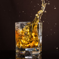 hexagonal glass of whiskey with ice and splashes from an abandoned and falling ice cube