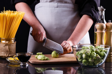 young woman cuts Brussels sprouts on a wooden cutting board