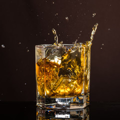 hexagonal glass of whiskey with ice and splashes from an abandoned and falling ice cube