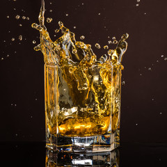 hexagonal glass of whiskey with ice and splashes from an abandoned and falling ice cube